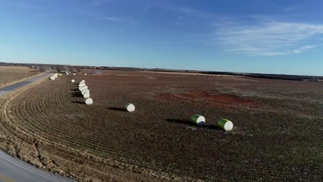 toma aérea de drones estáticos de una granja de algodón del medio oeste con pacas frescas de algodón cosechado envuelto en material amarillo brillante contra un cielo azul abierto