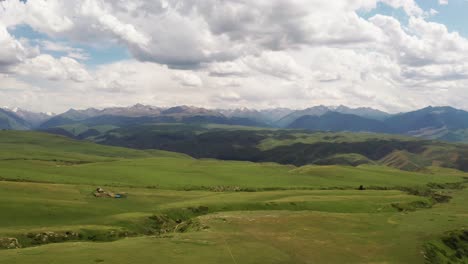 mountain peaks and grassland are under white clouds.