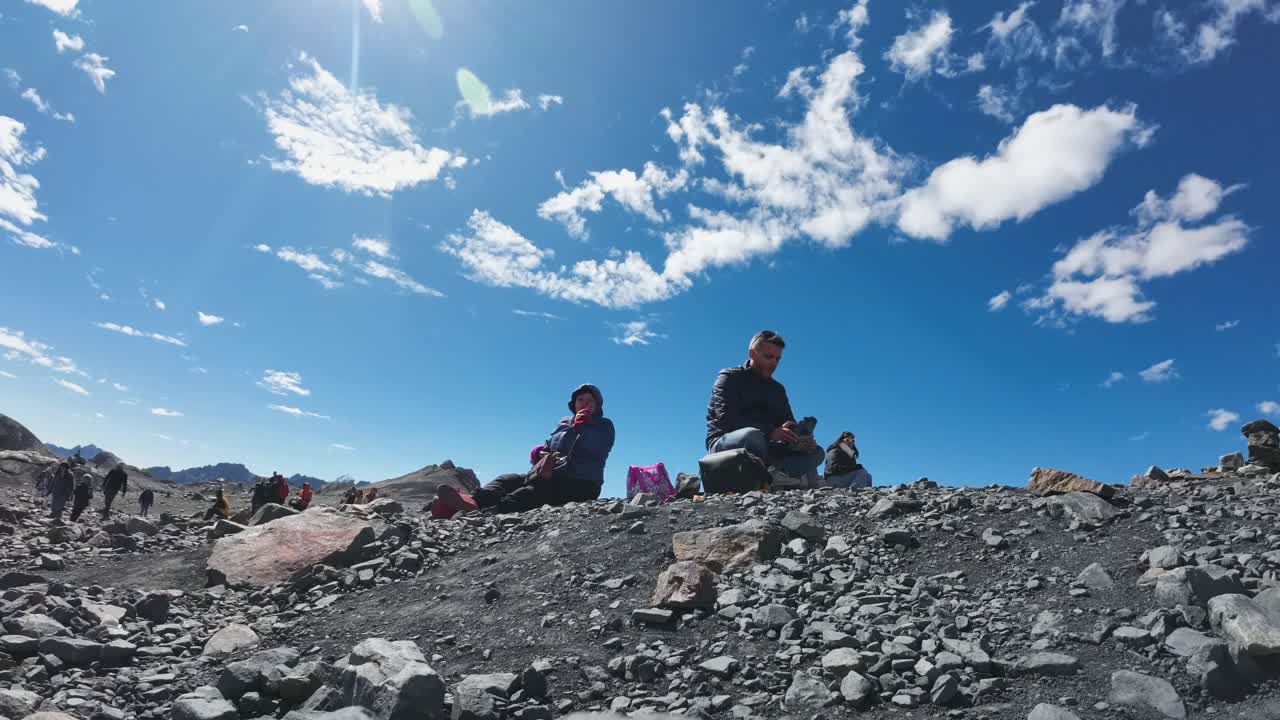Persone che si riposano e camminano su un terreno roccioso di montagna sotto un cielo blu