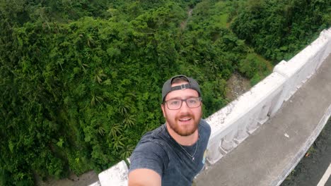 a handsome tourist taking a selfie or recording a video while standing in agas-agas bridge with background of lush foliage in sogod, southern leyte, philippines. - handheld shot