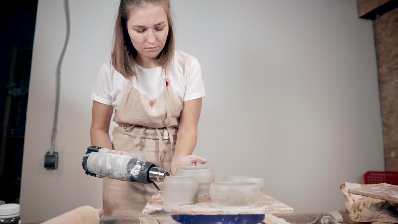 mujer usando una herramienta de aire caliente para secar cuencos de arcilla