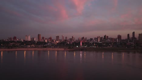 drone pan right showing asunción skyline at golden hour with colorful sunset clouds and water reflections