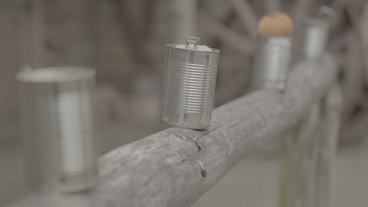 Tin or metal can getting shot off a wooden bar near a western village and falling down in slowmotion with a focus shift to a wooden wheel LOG