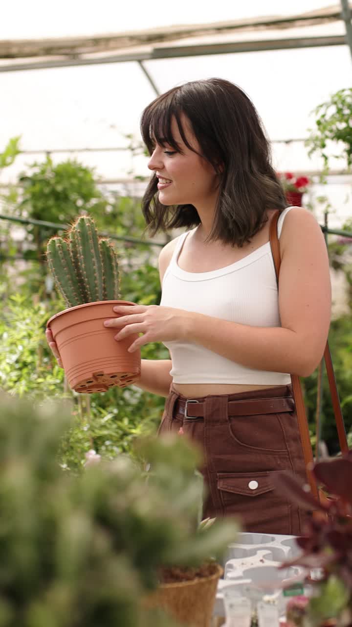 Woman choosing cactus in garden center. Vertical