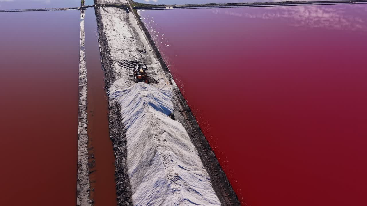 Salt piles in industrial area near red water under clear sky