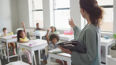 video of caucasian female teacher holding documents and teaching in class of diverse pupils