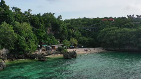 Tourists-relaxing-in-turquoise-blue-ocean-at-Padang-Padang-beach-in-Uluwatu-Bali,-aerial