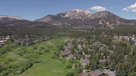 4k drone footage pan to the left of beautiful mammoth mountain in the summertime with a view of a lush green meadow and cabins