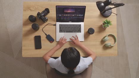 top view of a woman color grading sitting in the workspace using a laptop next to the camera editing the video at home