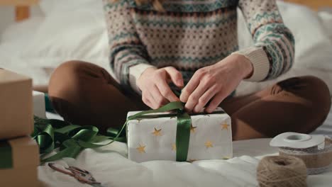 tilt up of unrecognizable caucasian woman sitting on bed and packing christmas gift at home.