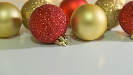 bolas de navidad rojas y doradas decoradas con brillo cerca de la mesa blanca con una guirnalda en el fondo