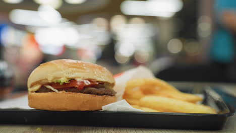 primer plano de papas fritas doradas y una hamburguesa en una bandeja negra en una mesa con un fondo borroso., destacando la deliciosa comida rápida en un entorno de comedor casual