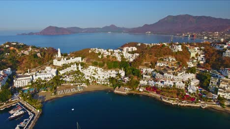 Aerial-View-of-Sailboats-near-Beach-Resorts-with-Mountains-and-Bay-Background