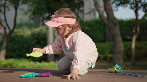 Kleines-Mädchen-Spielt-Allein-Mit-Bunten-Angelspielzeugen-Auf-Dem-Boden-Im-Park