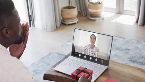 Hombre-Afroamericano-Sosteniendo-Un-Regalo-Y-Hablando-Con-Una-Mujer-Birracial-En-La-Pantalla-Del-Portátil