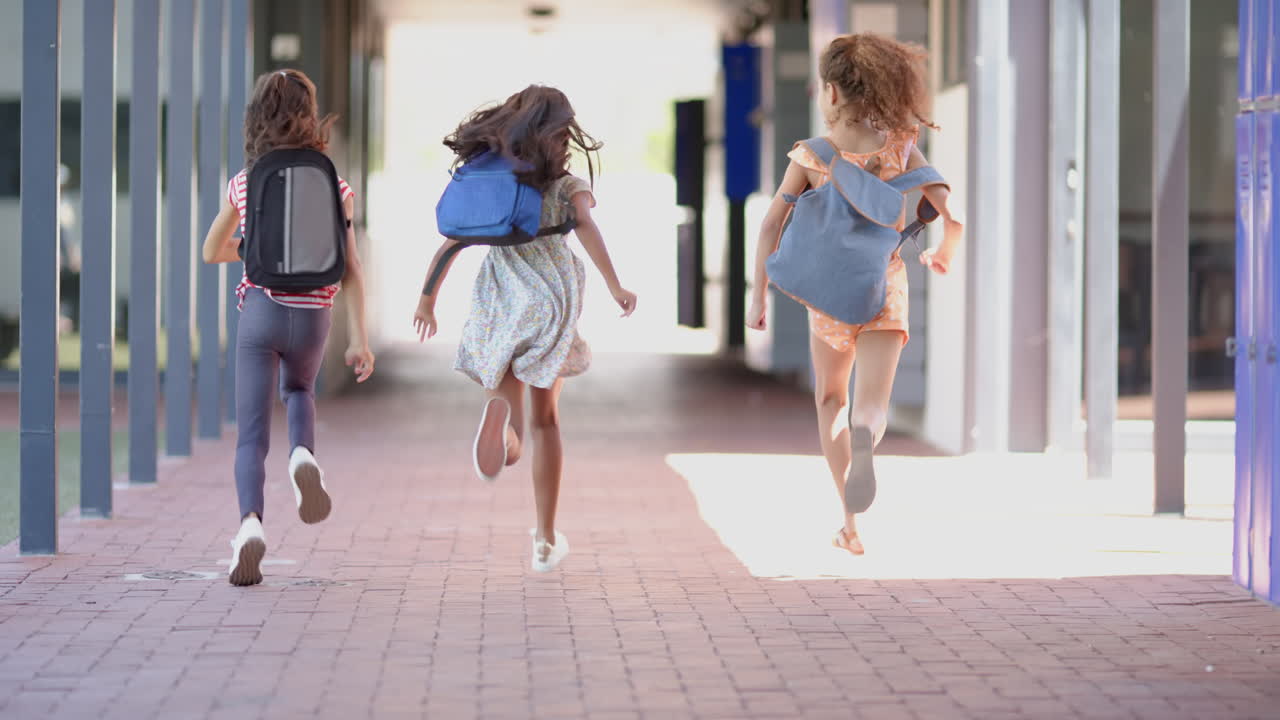 Three biracial girls are running joyfully with backpacks in school