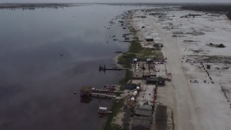 A-drone-shot-moving-along-the-shore-of-the-Dakar-pink-lake,-showing-the-mounds-of-salt-and-the-boat-used-for-the-extraction