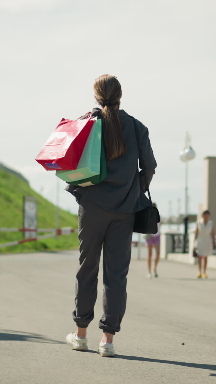 회색 옷을 입은 여자가 어깨에 쇼핑 가방을 들고 걸어가고, 사람들이 주차된 자전거와 함께 다리의 가장자리에 서 있습니다.