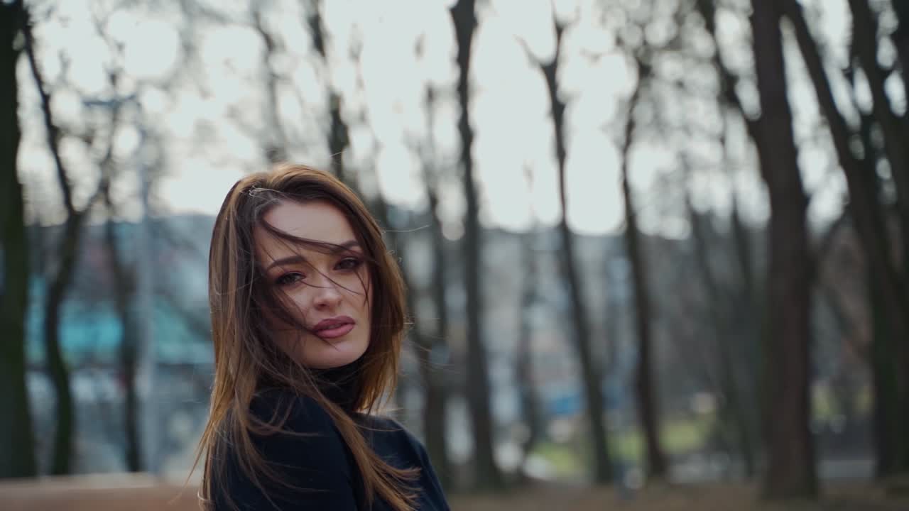 Portrait of charming young woman on the city park background. Beautiful model posing on camera outdoors. Motion camera around.