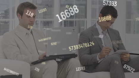 multiple changing numbers floating against two business using laptop and taking notes