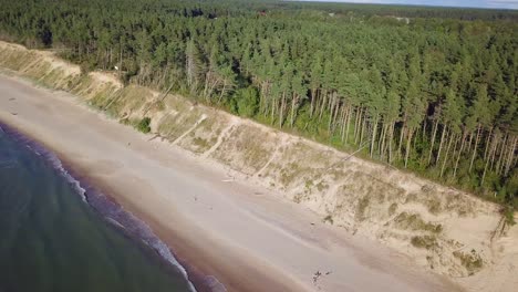 Luftbild-Aus-Der-Vogelperspektive-Auf-Den-Ostseestrand-Von-Jurkalne-An-Einem-Sonnigen-Tag,-Weiße-Sandklippe,-Die-Durch-Wellen-Beschädigt-Wurde,-Küstenerosion,-Klimaveränderungen,-Weitwinkeldrohnenaufnahme,-Die-Sich-Hoch-Nach-Vorne-Bewegt