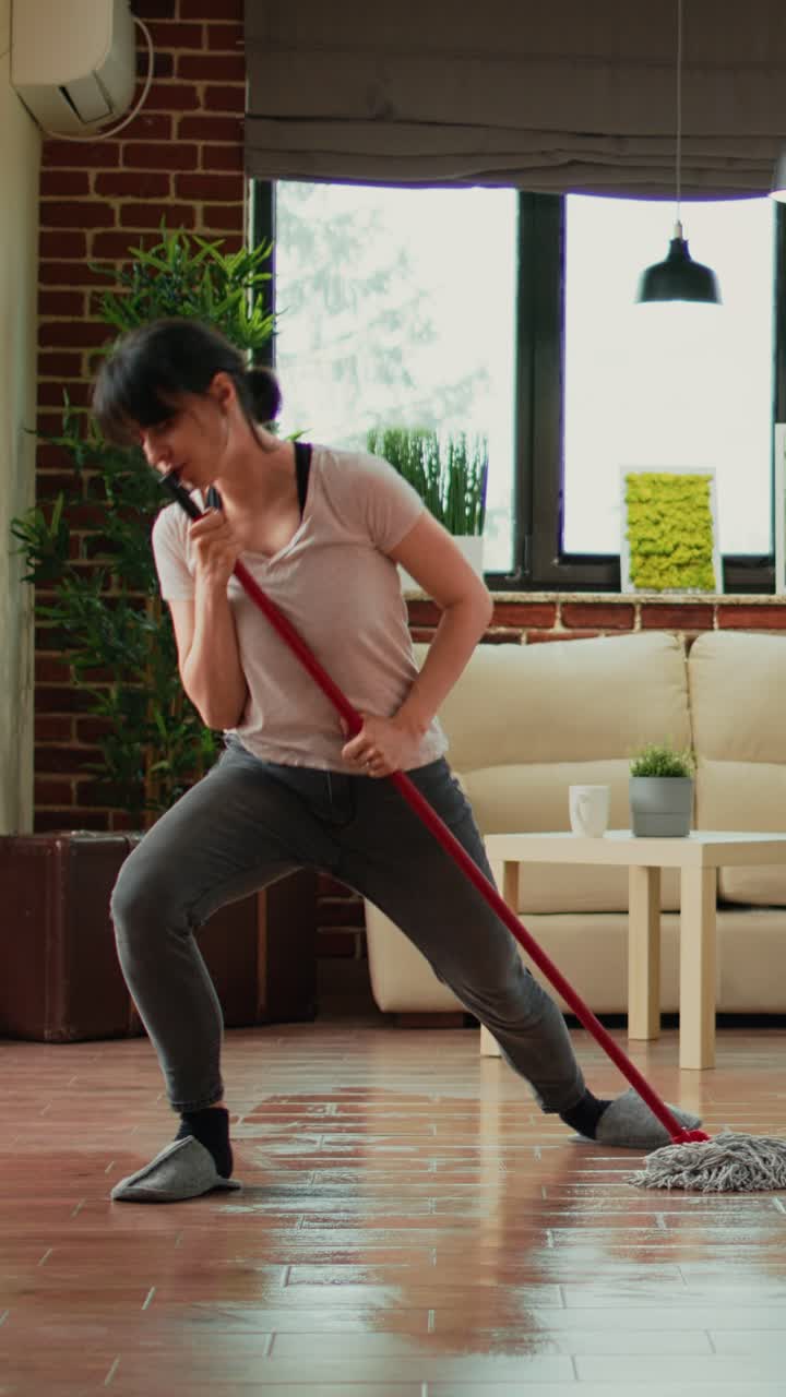 Vertical video: Caucasian wife cleaning apartment floors with mop
