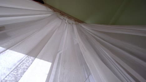 una cortina transparente en la ventana, ligeramente balanceándose en el viento en la habitación.