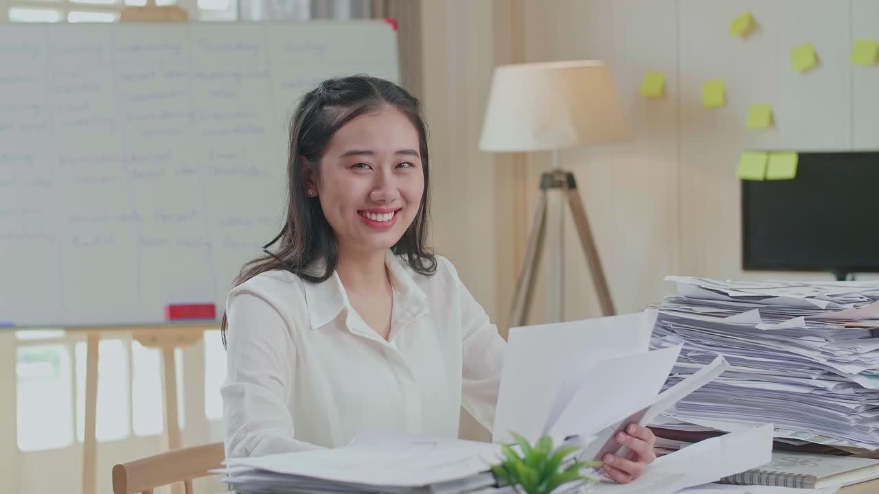 Asian Woman Smiling To Camera While Working With Documents At The Office