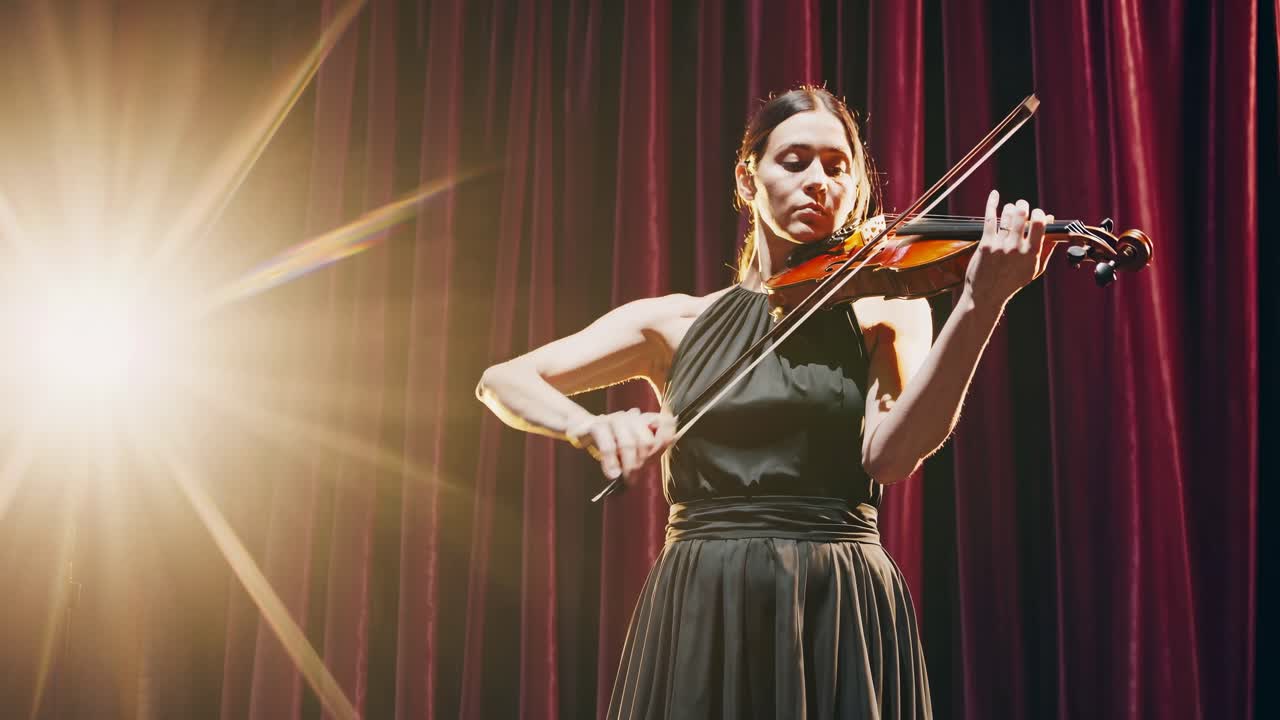 A violinist performs on stage, illuminated by spotlight, captured from a low-angle