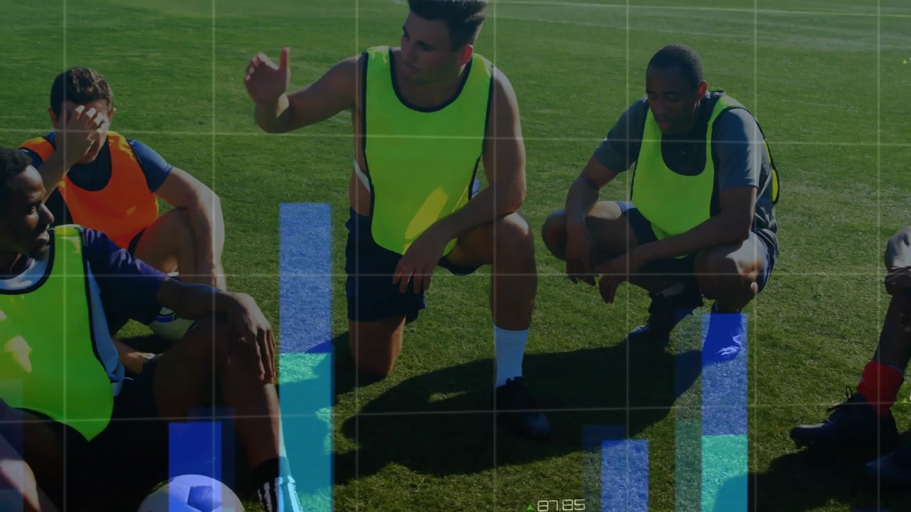Gathering soccer team kneeling gesturing talking on sunny pitch with neon bibs ball data overlays