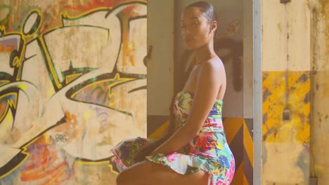 chica caribeña se pone en cuclillas en su vestido de flores con graffiti en la pared en el fondo