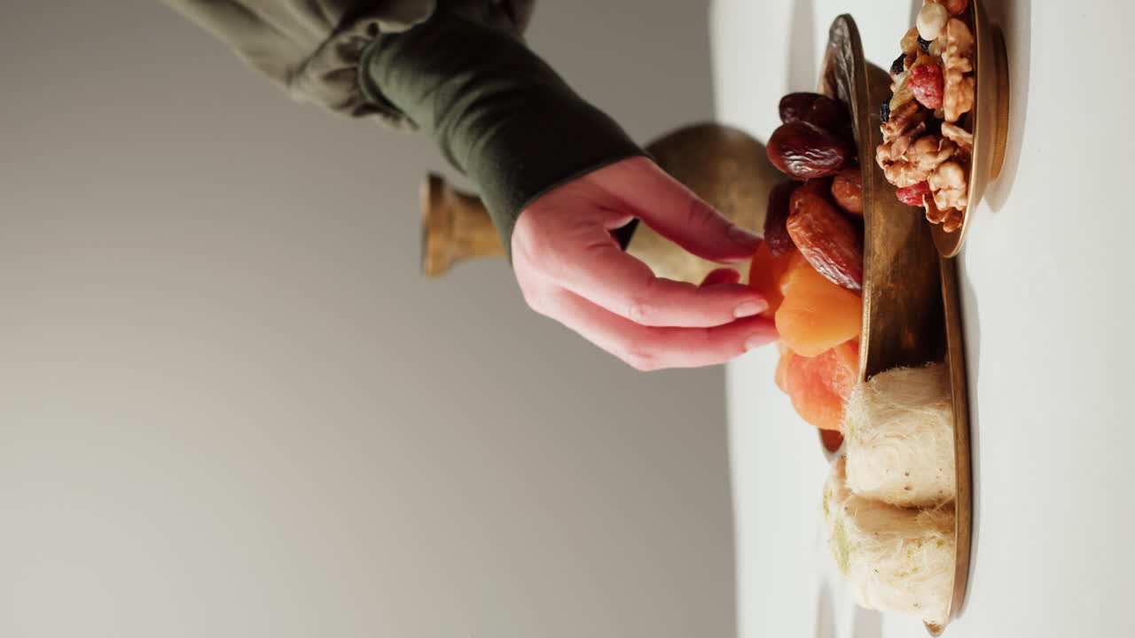 Hand reaching for dried fruit and sweets on a brass tray.