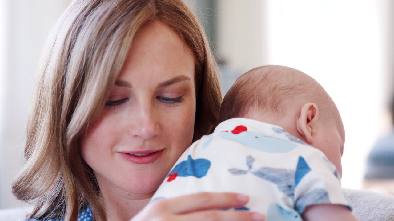 집 에서 소파 에 앉아 피곤 한 아기 아들 을  ⁇ 안고 있는 어머니 의 느린 동작 촬영