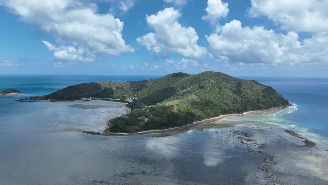 Rekaman pelacakan drone lambat di siang hari, bergerak menyamping di sepanjang garis pantai Pulau Hayman untuk memperlihatkan dataran karang dangkal, garis pantai berpasir, dan laut lepas, Whitsundays, Queensland, Australia