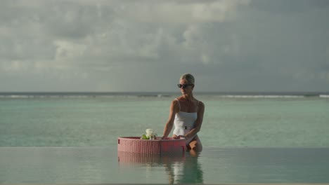 Mujer-Sentada-En-El-Borde-De-La-Piscina-Infinita-Disfrutando-De-Una-Bebida-Del-Desayuno-Flotante