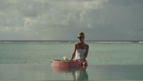 woman sitting on infinity pool edge enjoying drink from floating breakfast