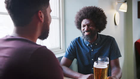 middle aged black father having a beer and talking with his adult son sitting at table in a pub, close up, dad facing camera