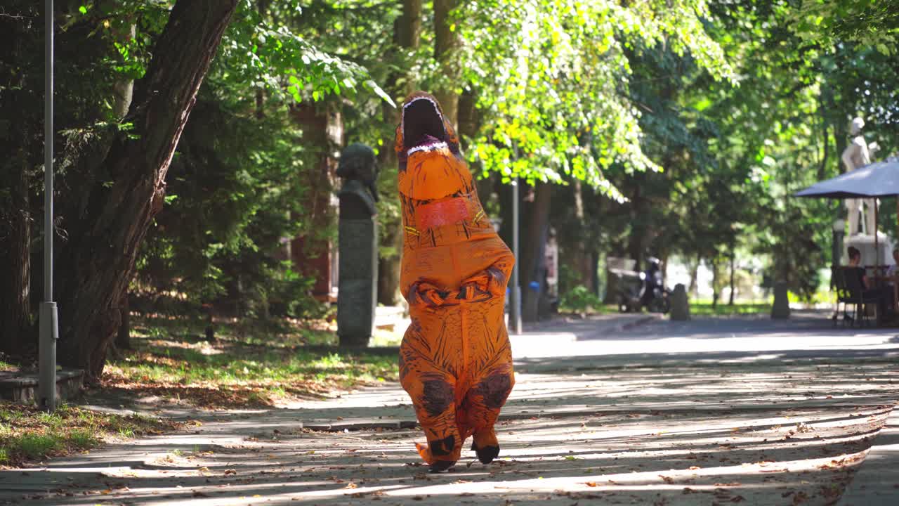 Funny dragon outdoors. Person dressed in an orange blow-up dragon costume walking in the park in a sunny day.