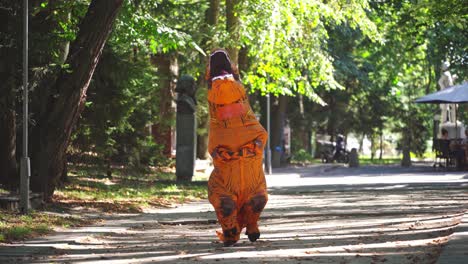 funny dragon outdoors. person dressed in an orange blow-up dragon costume walking in the park in a sunny day.