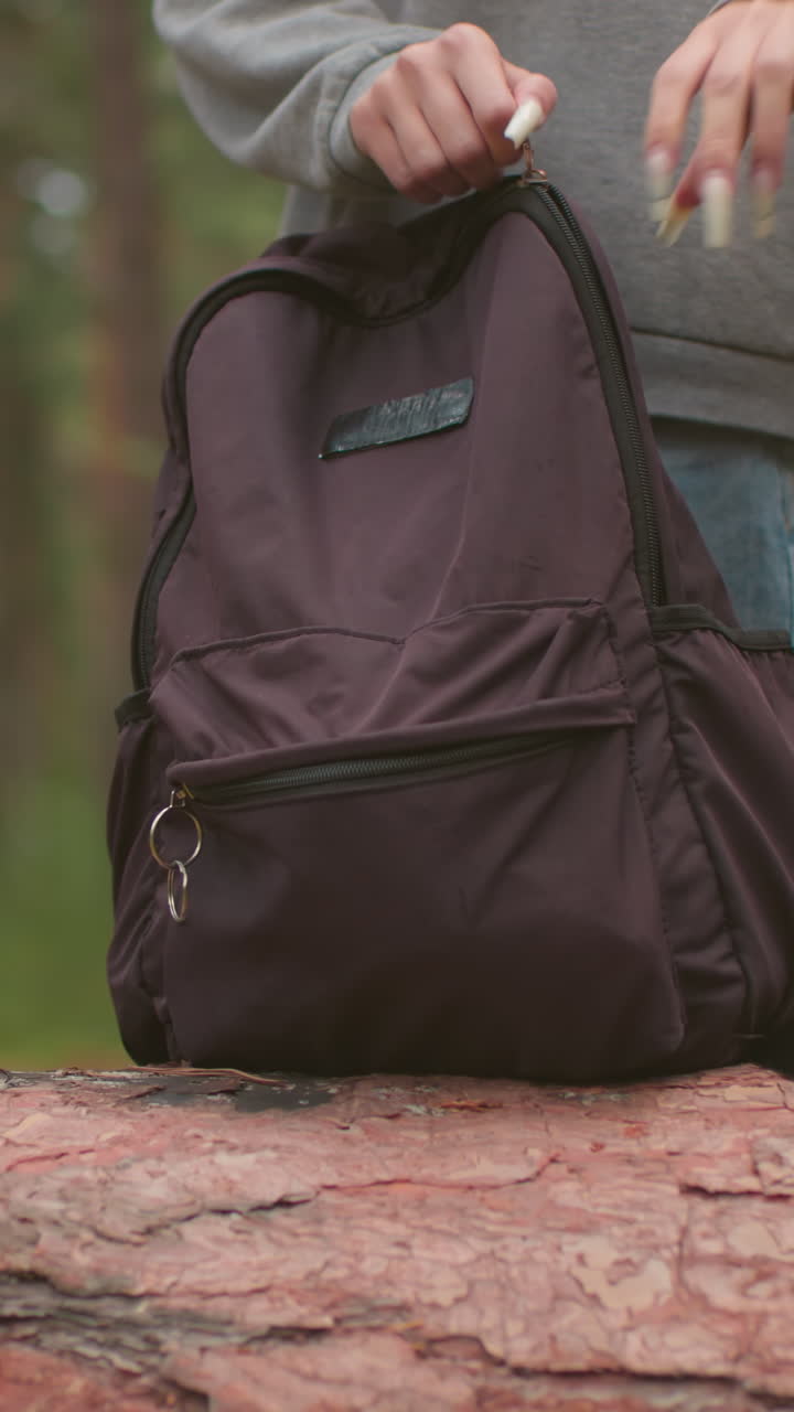 두 명의 젊은 산책객이 조용한 숲을 걸어, 배을 들고 풍경을 감상하고, 그들은 쓰러진 나무에 접근하고, 회색 스웨터를 입은 여자가 그녀의 검은 가방을 열기 시작합니다.