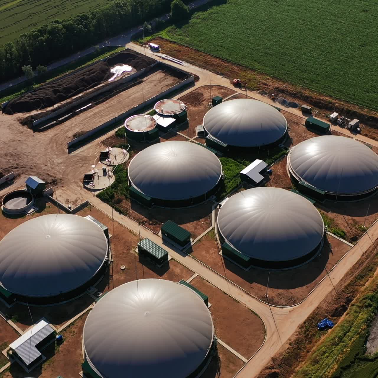 Grey round tops of fuel reservoirs of biogas plant. Organic production of safe energy. Aerial view. Green fields at the backdrop