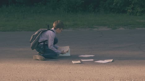 schoolboy-gathers-books-and-sheets-in-trees-shadow