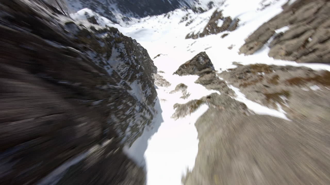 Drone da corsa in volo sopra montagne rocciose coperte di neve, Pirenei