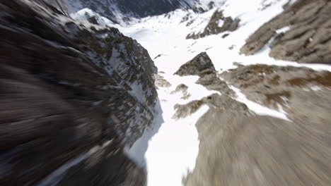 Racing-drone-flying-over-rocky-mountains-covered-with-snow,-Pyrenees