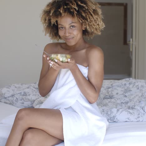 mujer joven en la cama comiendo ensalada de verduras