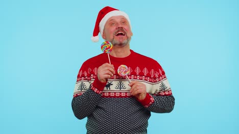 funny man in red christmas sweater holding candy striped lollipops hiding behind them fooling around