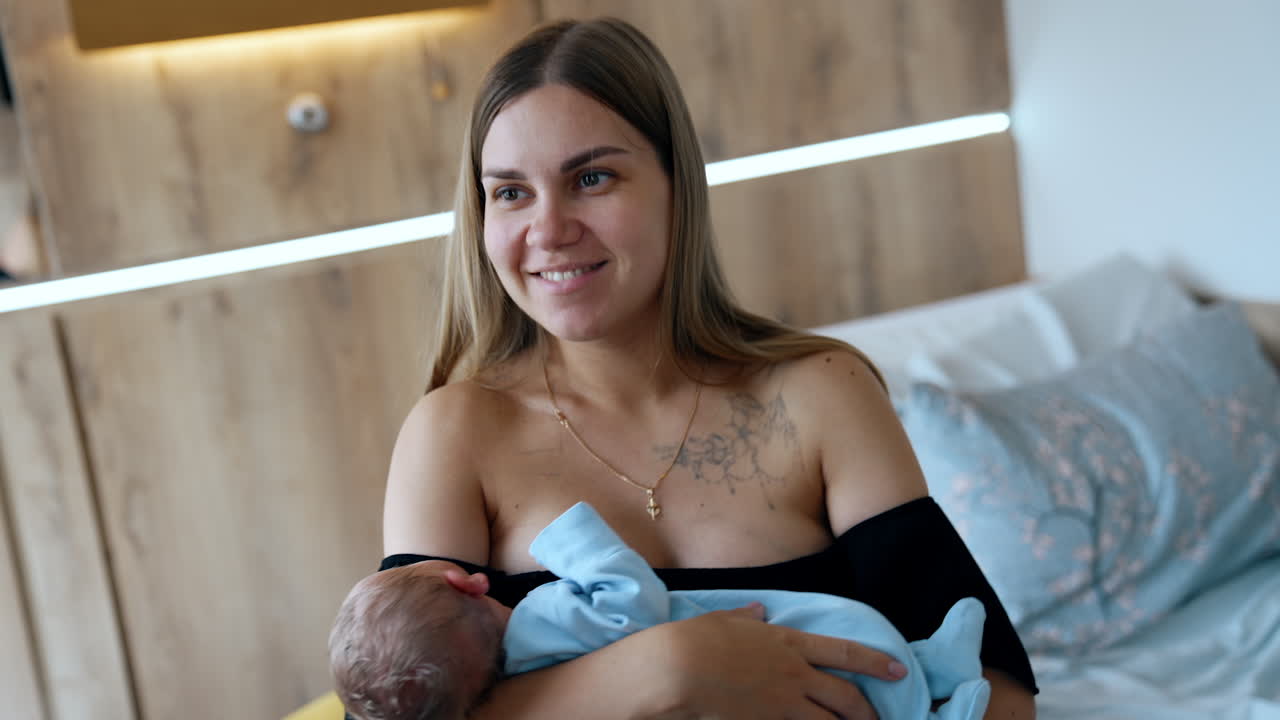 Happy smiling Caucasian woman in black dress with bare shoulders holding a baby. Smiling mother waving her tiny newborn son.
