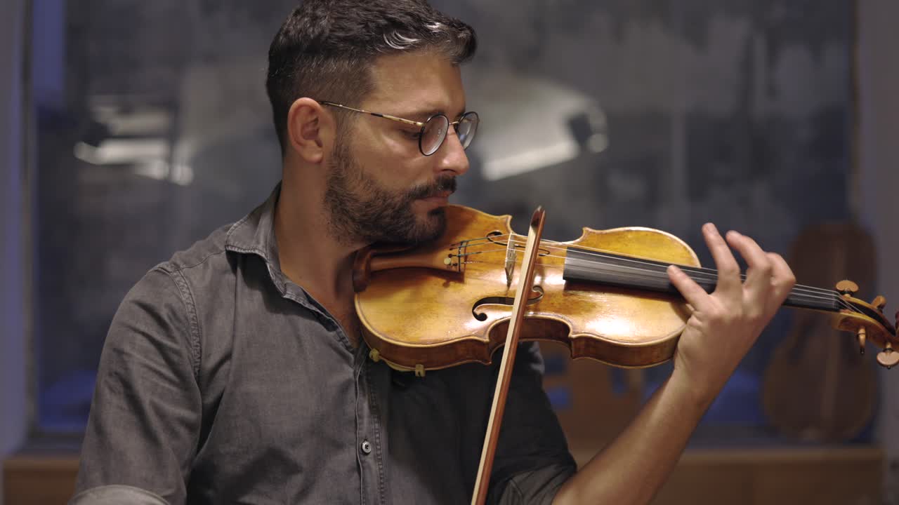 un luthier barbudo adulto tocando un violín hecho a mano