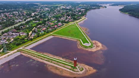 Majestic drone shot showing Ogres lighthouse on riverbank near lush town