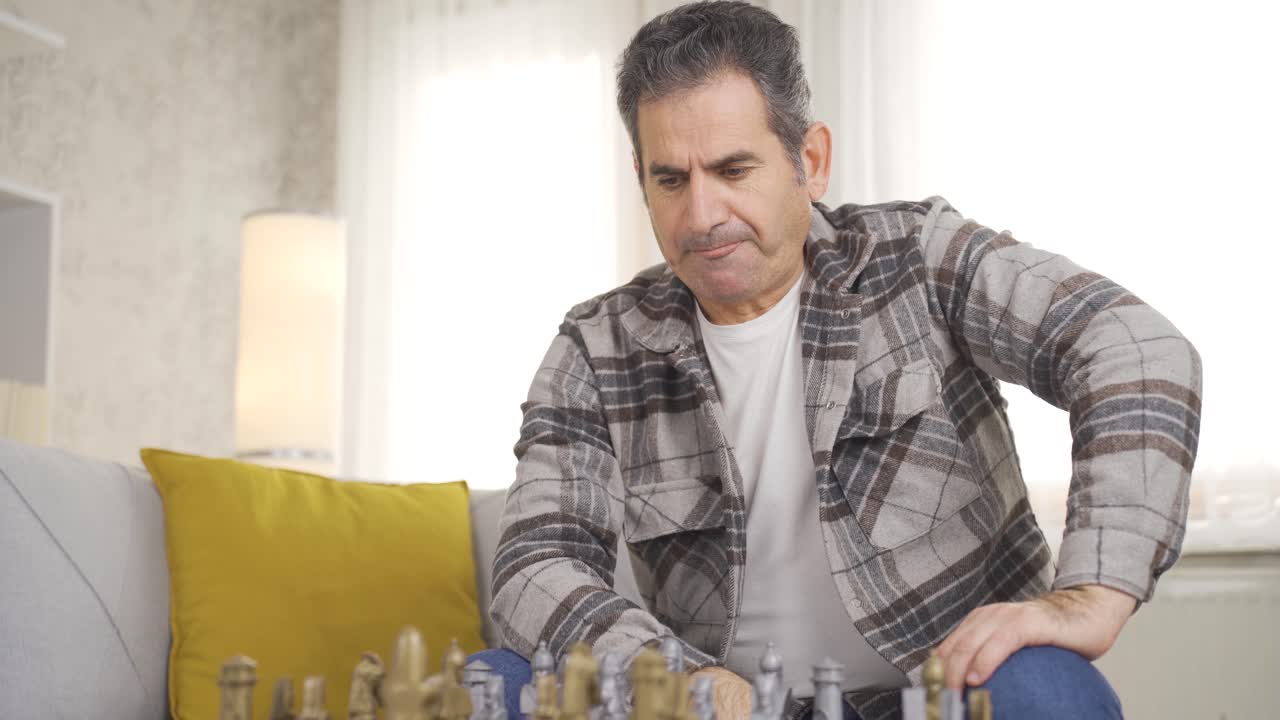 hombre maduro sentado en el sofá en casa jugando al ajedrez pensativo solo.